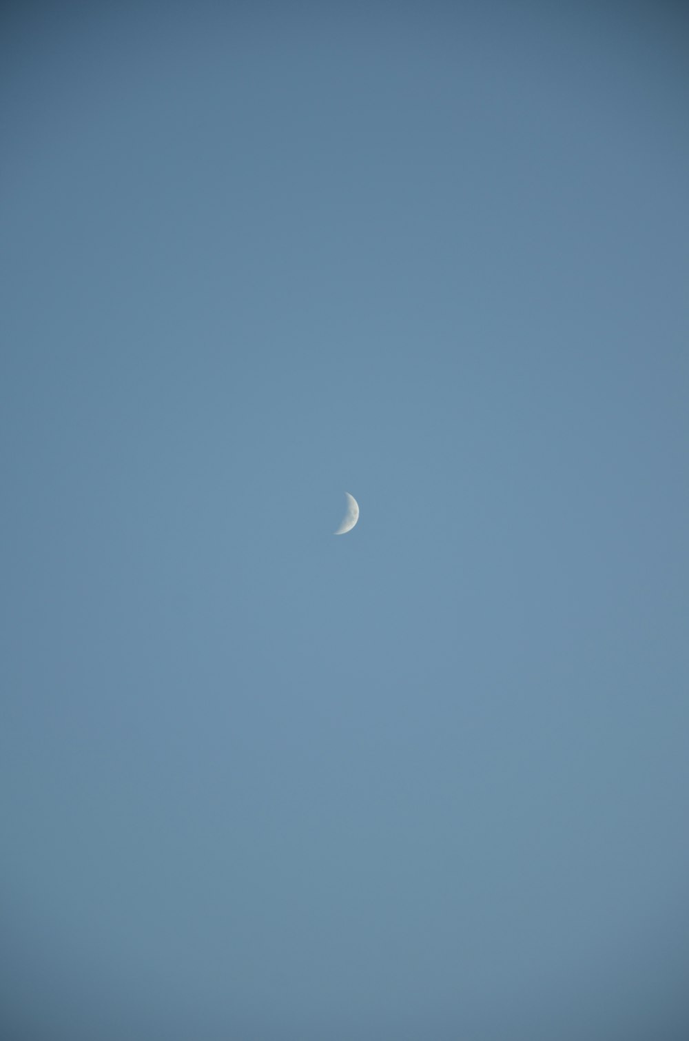 a half moon is seen in a clear blue sky