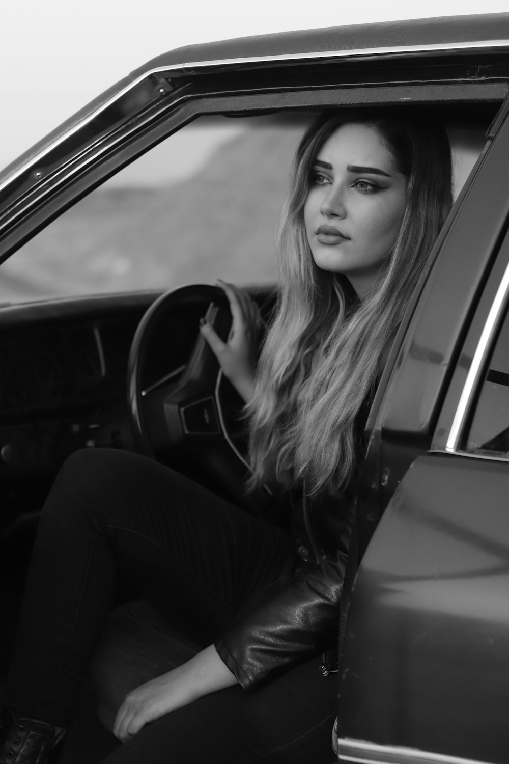 a woman sitting in a car with her hand on the steering wheel