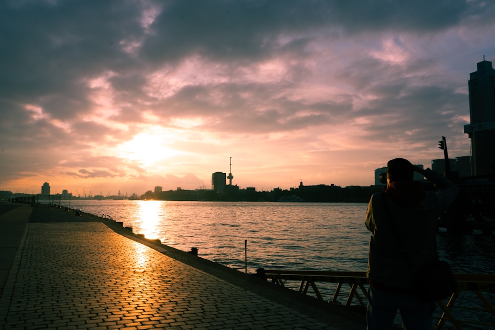 a person taking a picture of the sun setting over a body of water