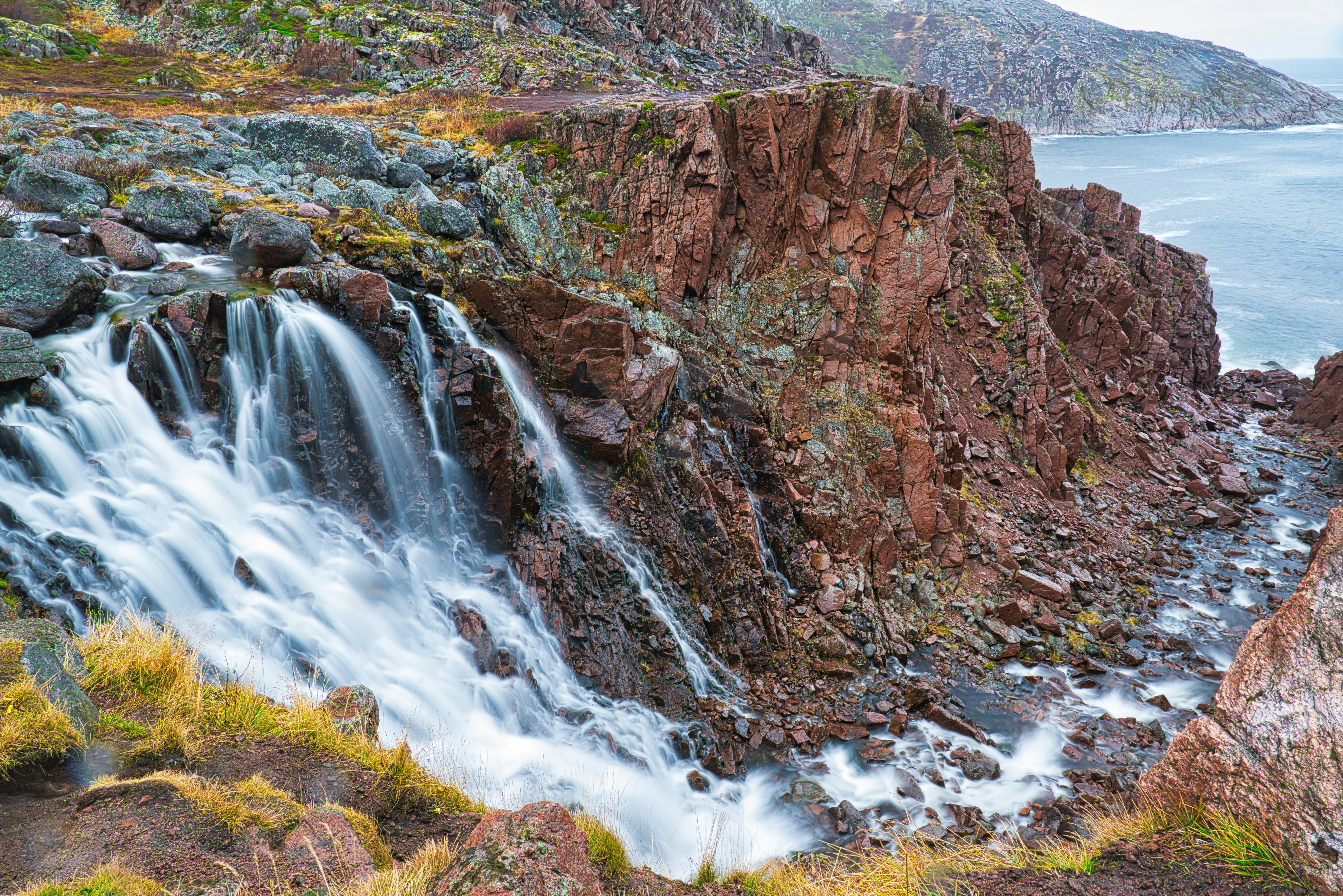 a waterfall in the middle of a rocky cliff next to the ocean