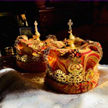 Close-up of antique gold ceremonial regalia with deep crimson accents displayed on a velvet cushion.