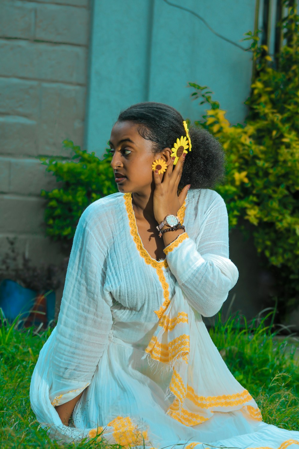 a woman sitting in the grass with a flower in her hair