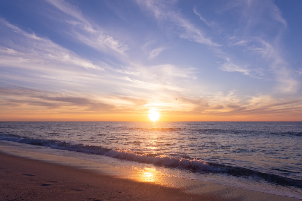 the sun is setting over the ocean on the beach