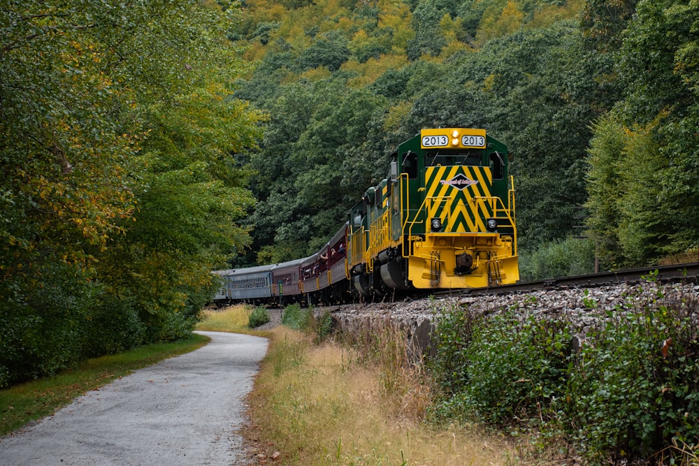 a yellow and green train traveling through a forest
