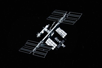 A large space station with multiple solar panels is floating against a backdrop of space. The station consists of several modular components and is symmetrical in design. The panels are arranged in a grid-like pattern, reflective of light.
