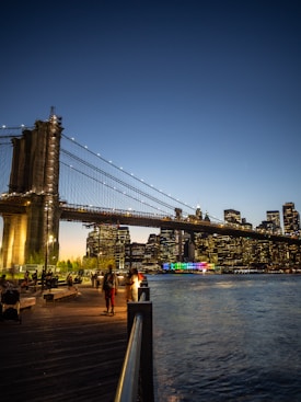people walking on a boardwalk near the water and a bridge