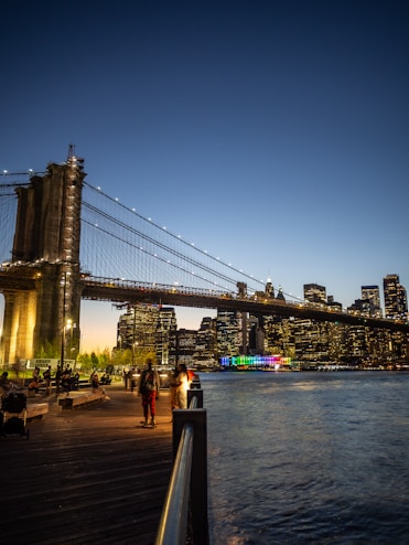 people walking on a boardwalk near the water and a bridge