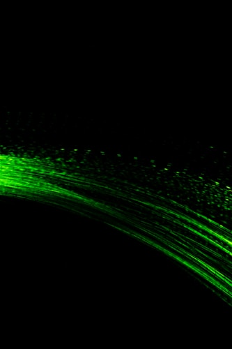 A dynamic display of vibrant green light trails arcs across a pitch-black background, resembling motion or energy in motion.