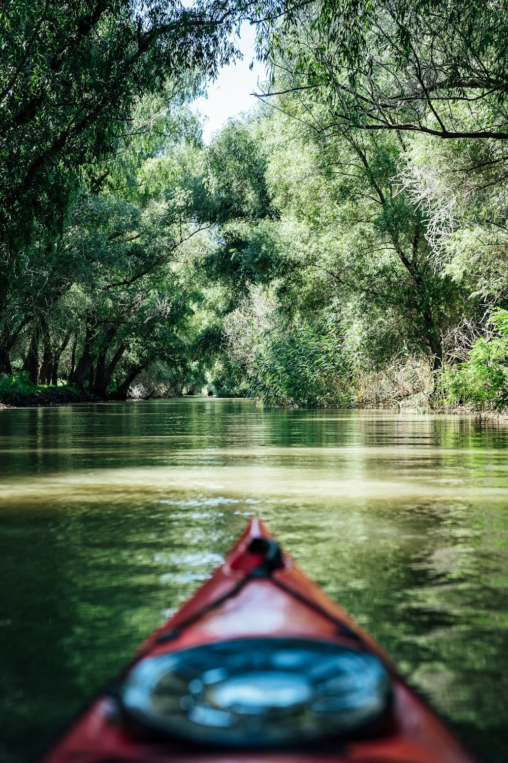 a red kayak floating down a river surrounded by trees