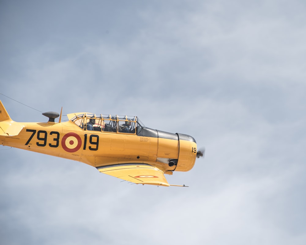 a small yellow airplane flying through a cloudy sky