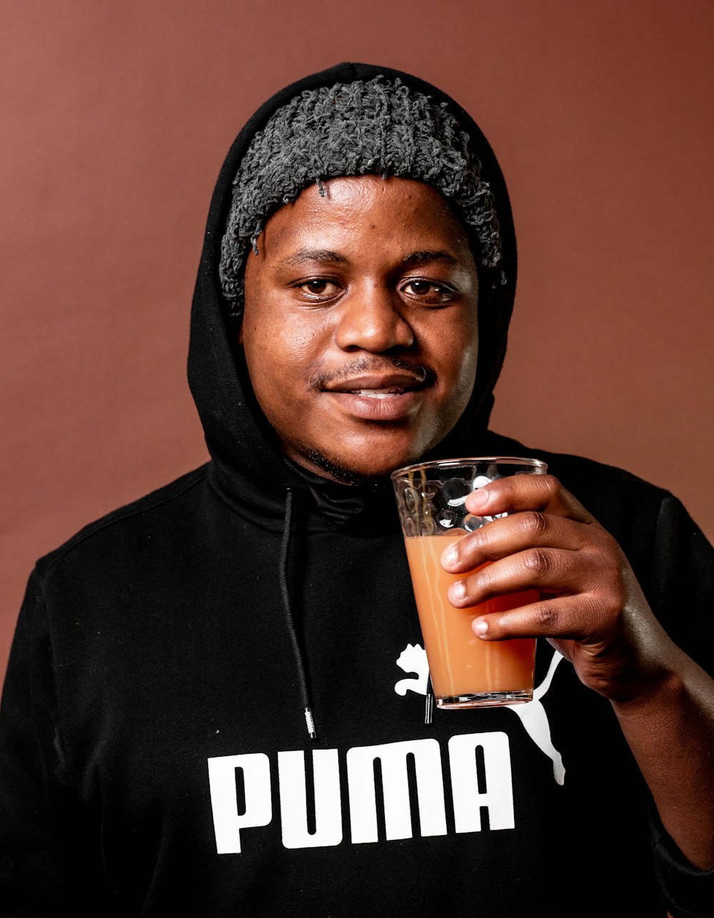 a man in a hoodie holding a glass of orange juice