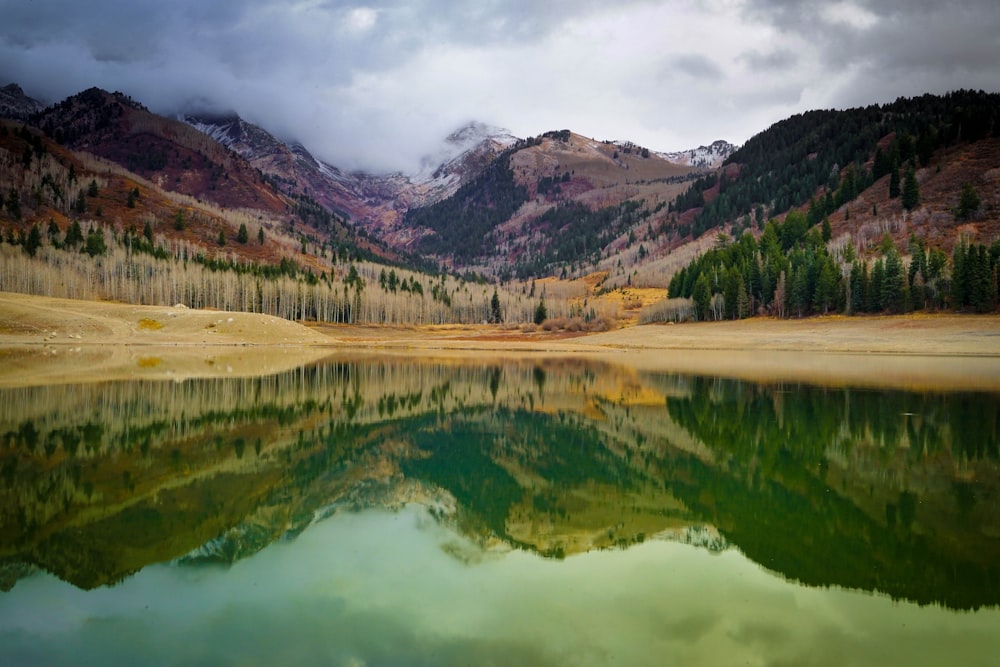 a lake surrounded by mountains and trees under a cloudy sky