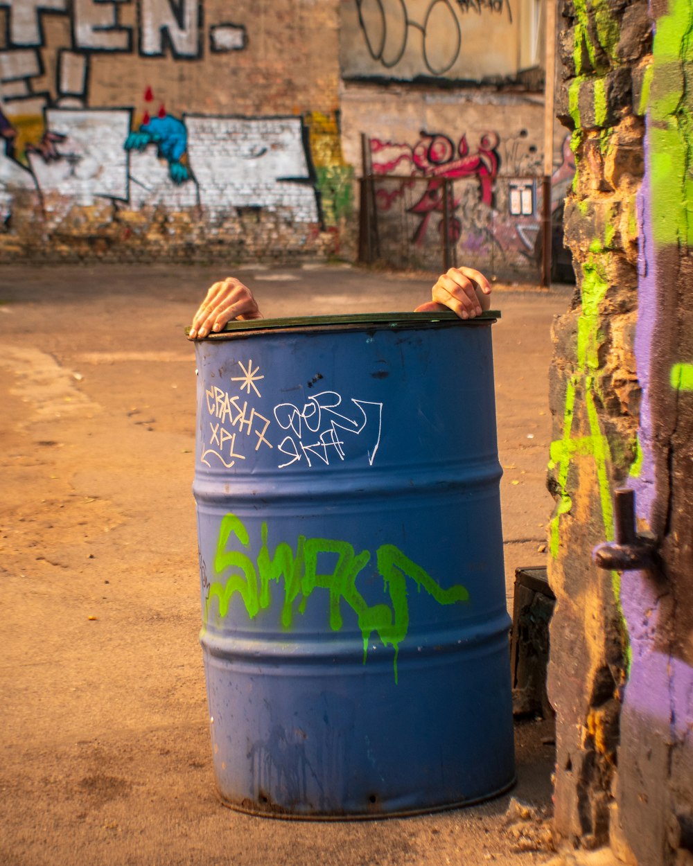 a blue barrel with graffiti on it next to a wall