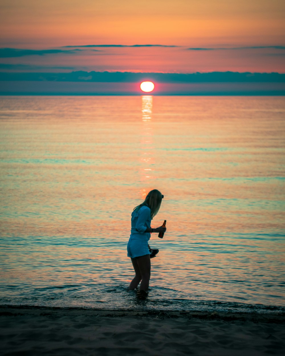 a woman standing in the ocean at sunset