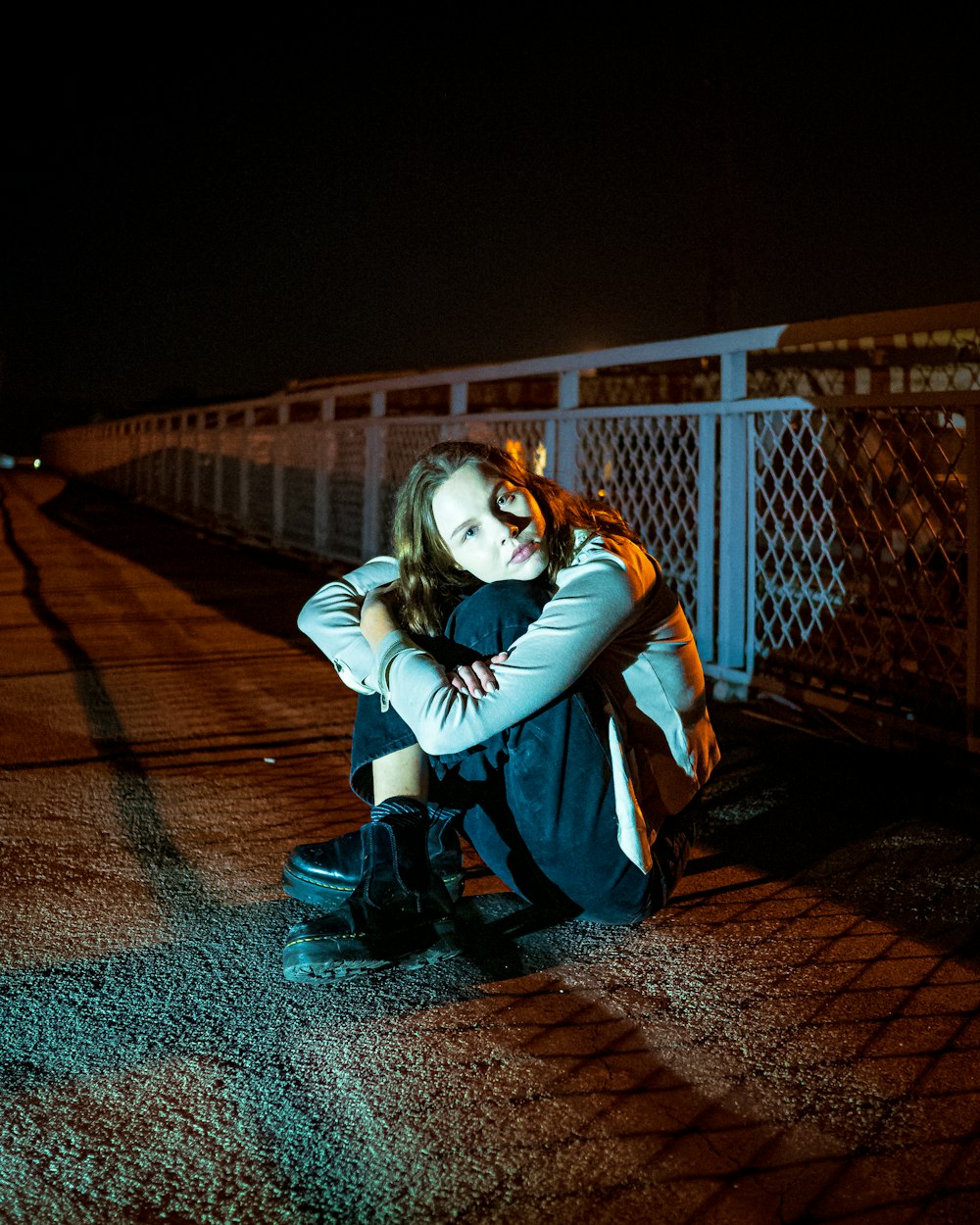 a woman sitting on the ground next to a fence