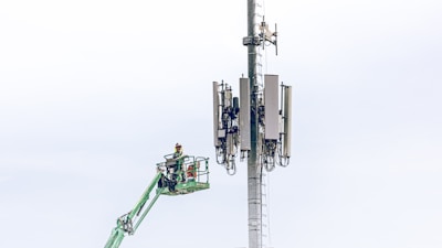 Close-up of communication equipment being adjusted on a 5G tower by a worker.