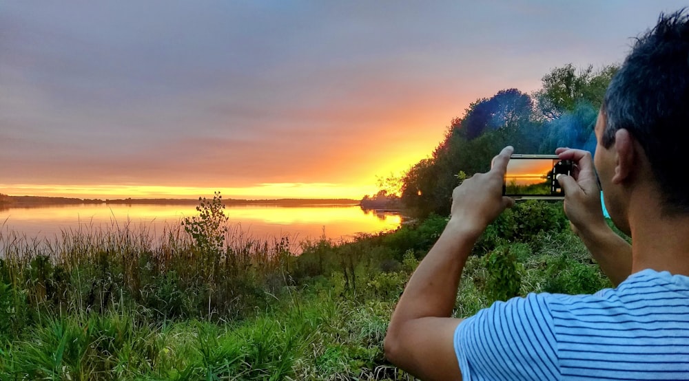 a man taking a picture of a sunset over a lake