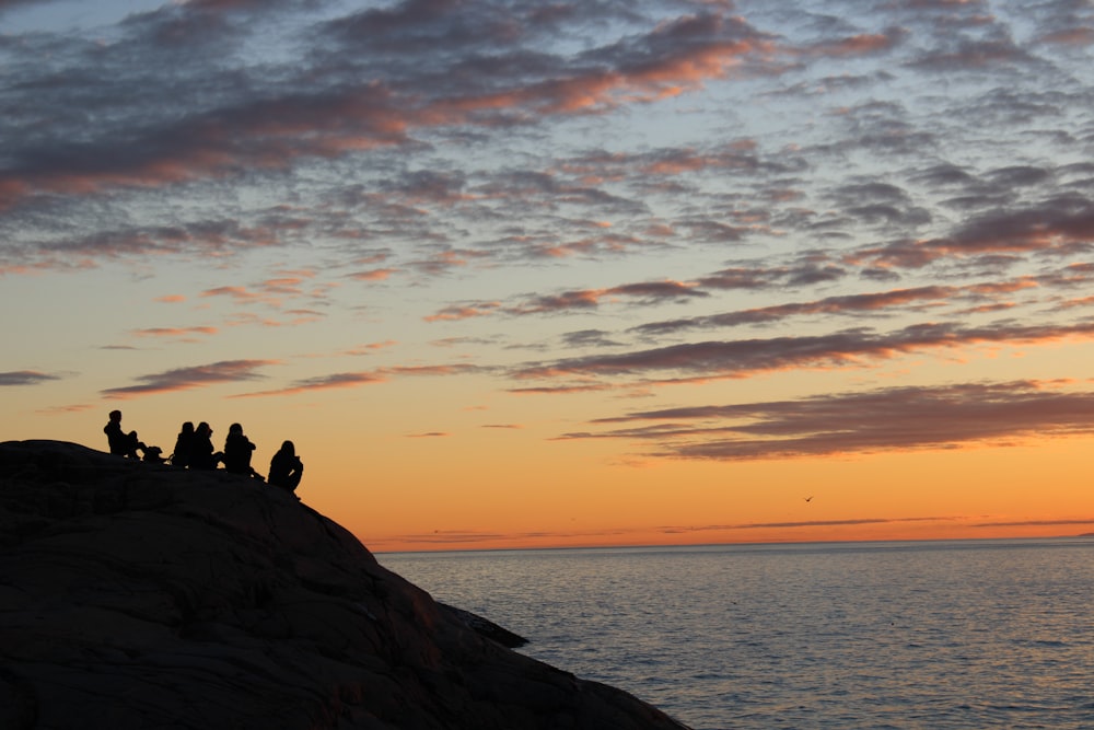 a group of people sitting on top of a rock next to the ocean