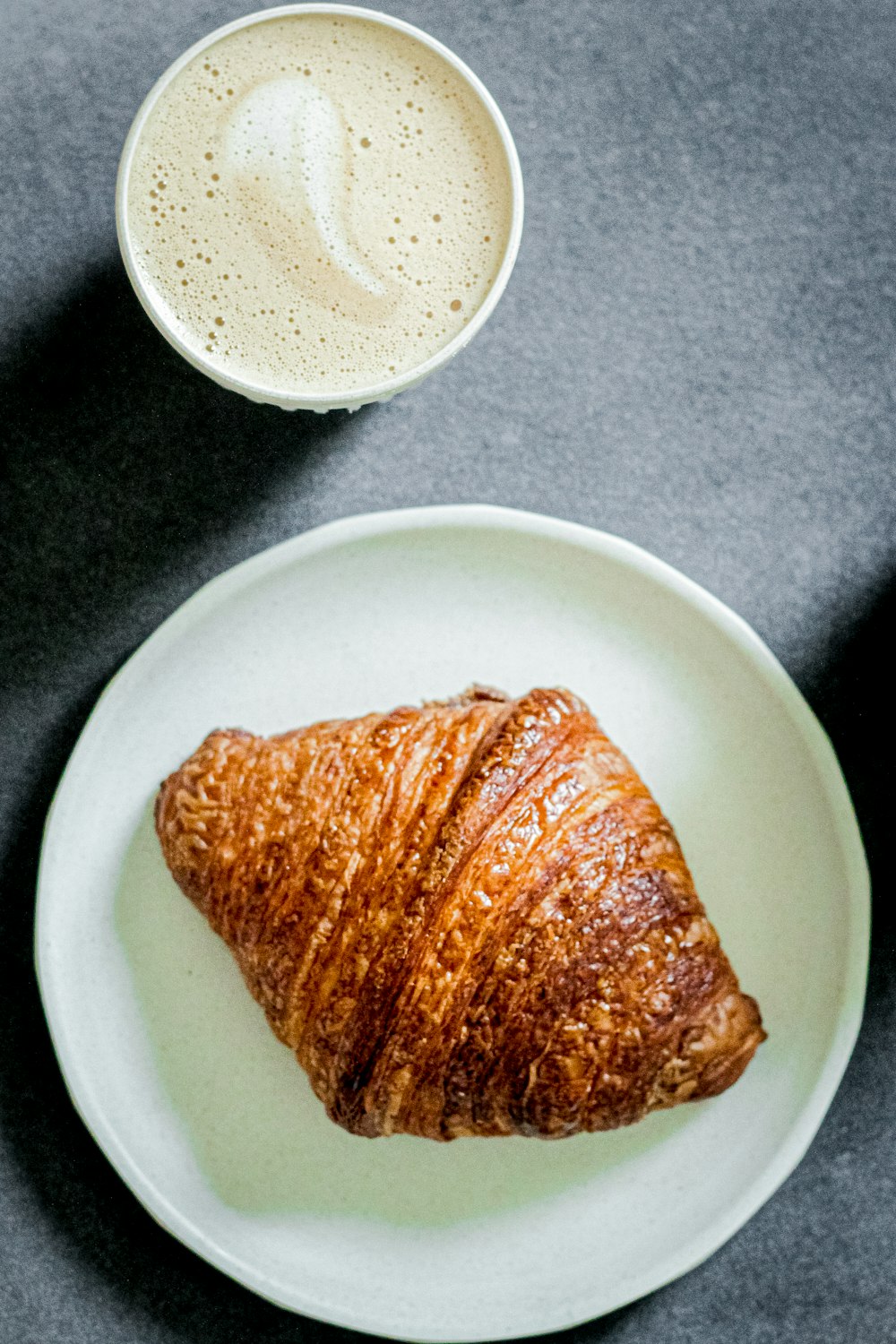 a croissant on a plate next to a cup of coffee