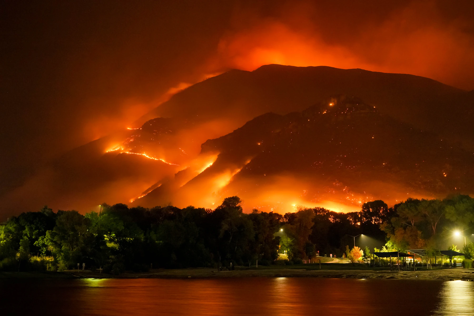A wildfire burning across mountains near a rural area
