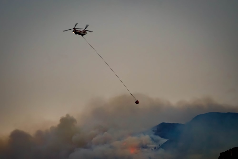 a helicopter flying through the air with a hose attached to it