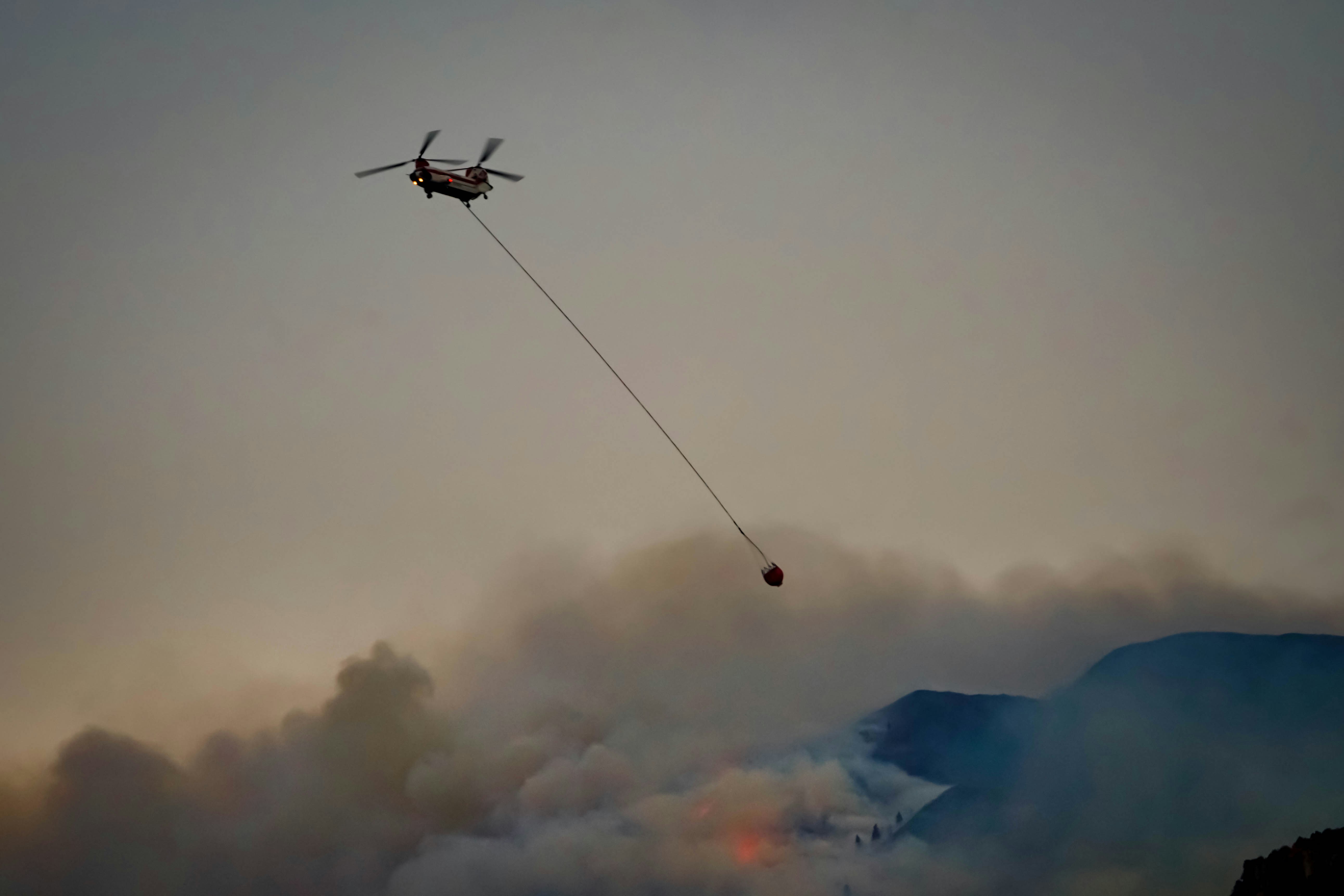 Large autonomous cargo drone spraying fire retardant over a forest fire at night