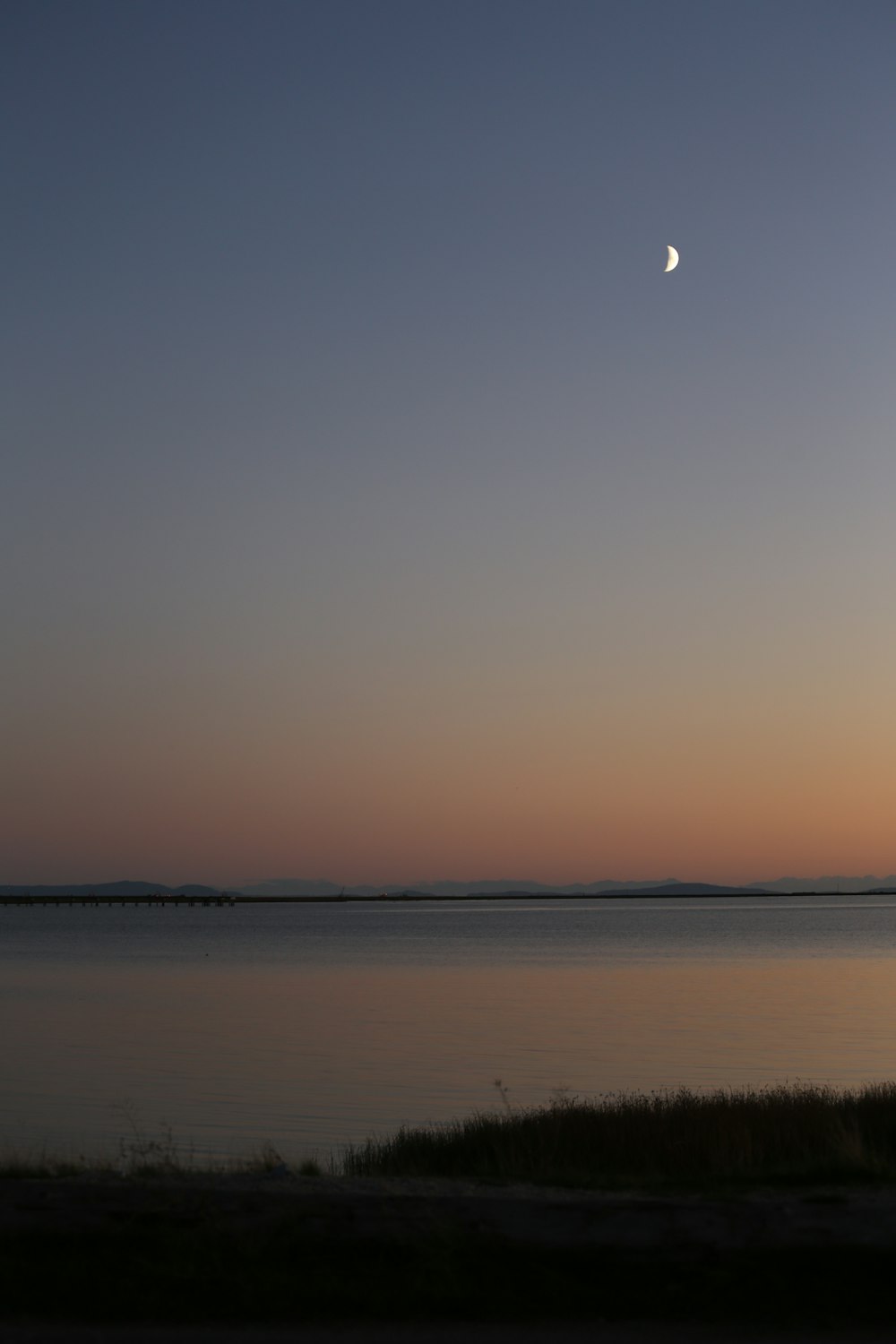 the moon is setting over a body of water