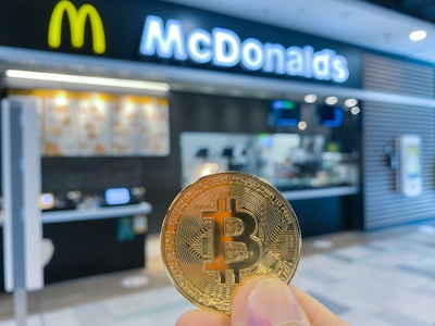 a hand holding a bit coin in front of a mcdonalds