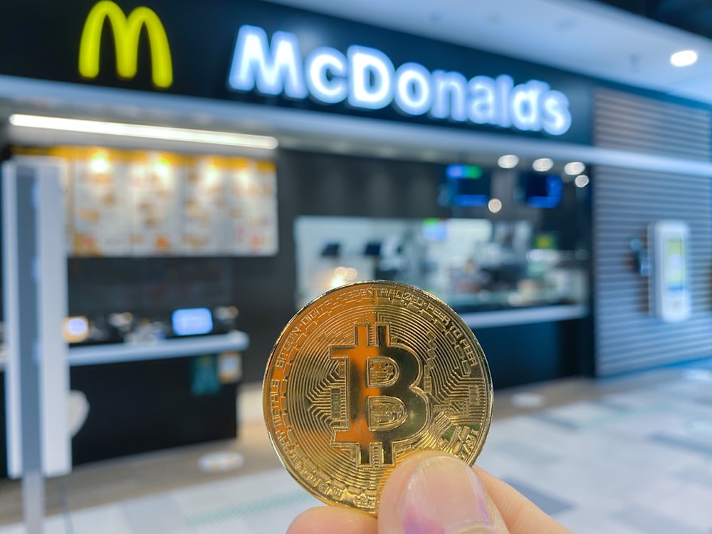 a hand holding a bit coin in front of a mcdonalds