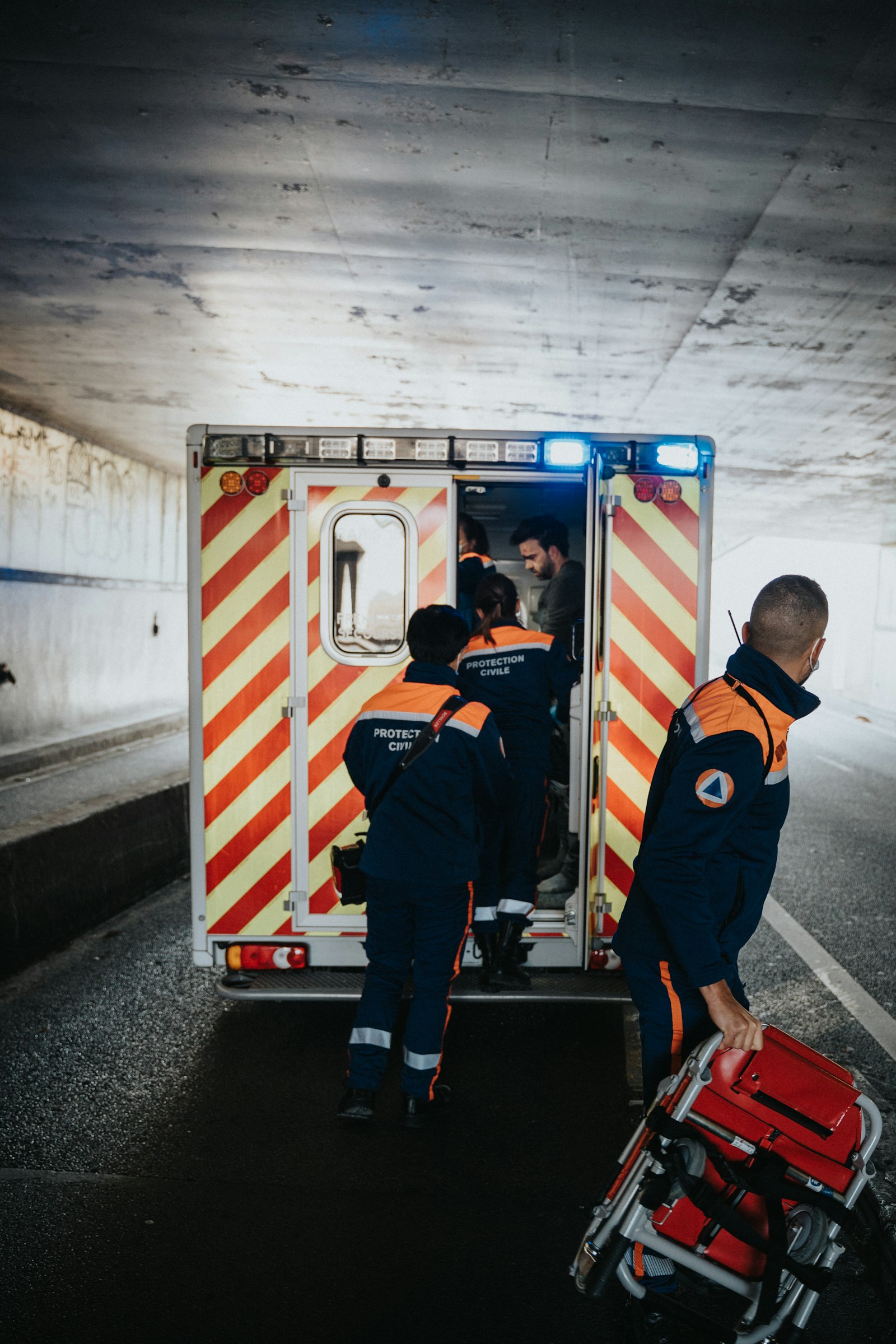 Two emergency medical crew members standing at the open back doors of an ambulance on a call