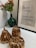 A decorative setting featuring a framed motivational quote next to a dark green vase with orange and green berry-like plants. Three shiny, metallic, copper-colored pumpkin sculptures rest on a white surface.