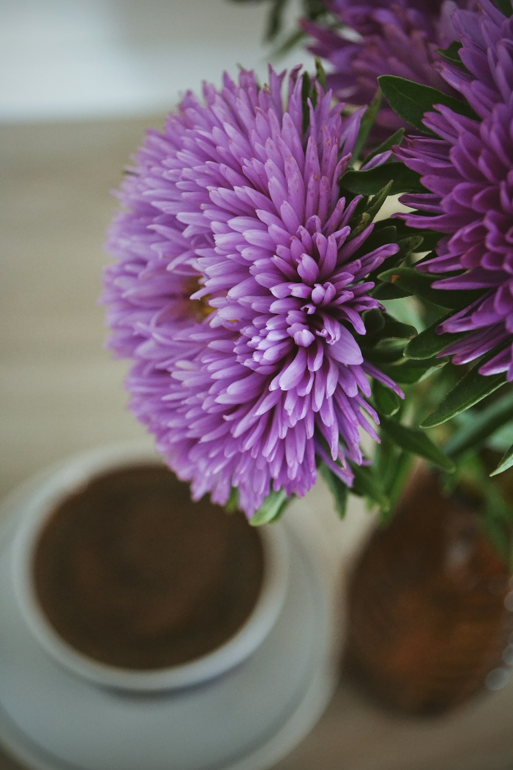 a vase filled with purple flowers next to a cup of coffee