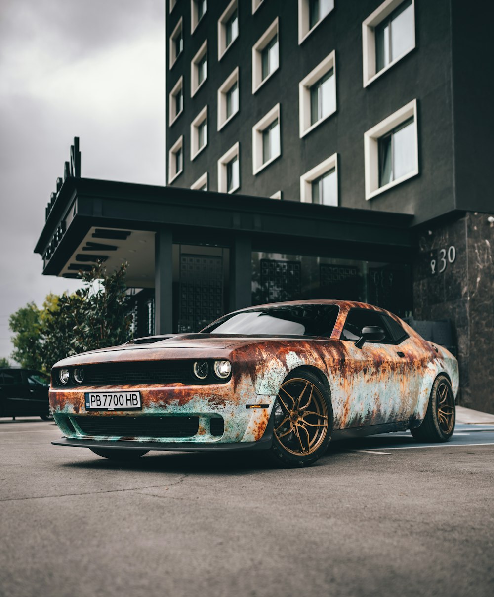 a rusted car parked in front of a tall building