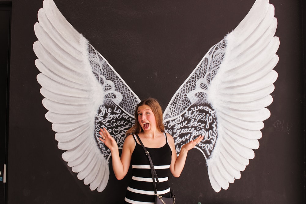 a woman standing in front of a wall with wings on it