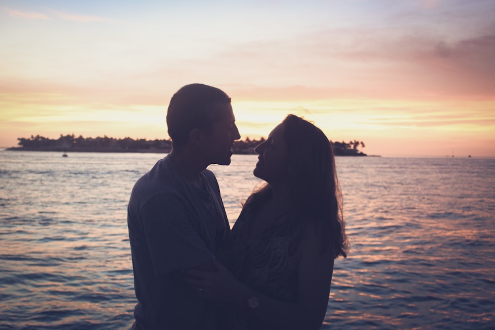 a man and woman standing next to each other near the ocean