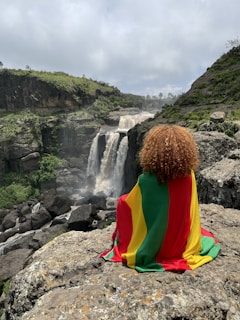a person sitting on a rock with a waterfall in the background