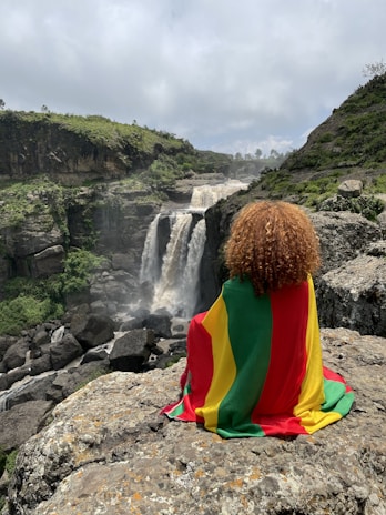 a person sitting on a rock with a waterfall in the background