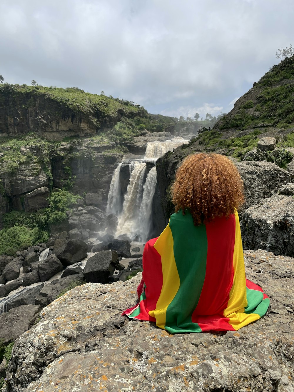 a person sitting on a rock with a waterfall in the background