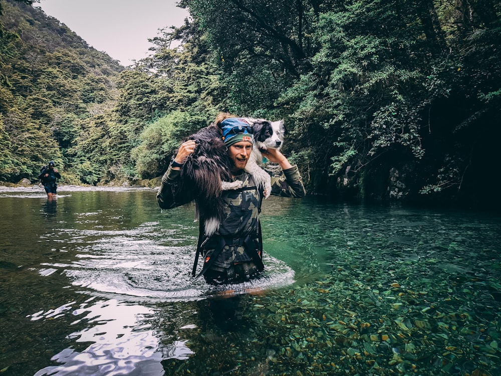 a woman is wading through a river with a dog on her back