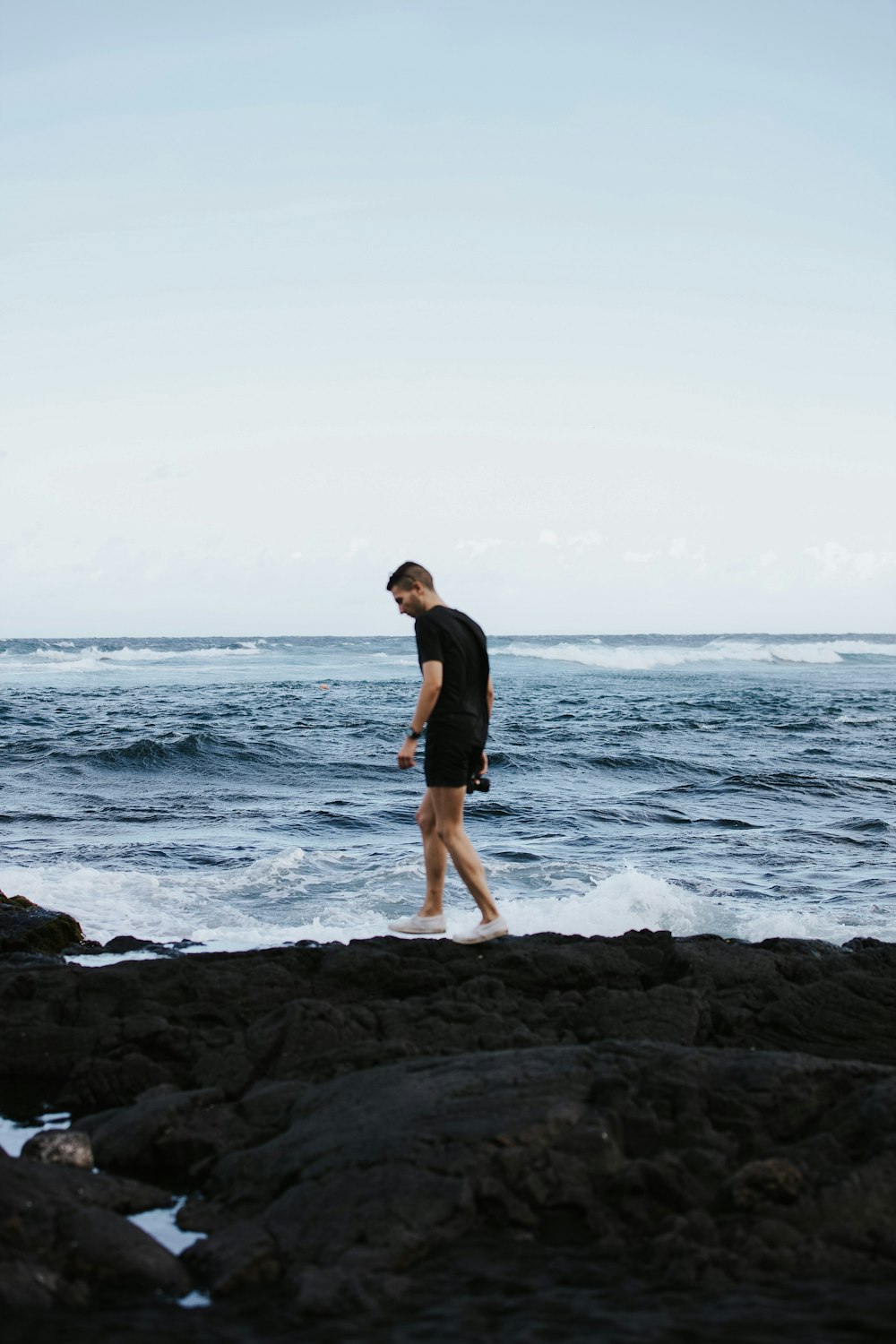 a man walking along a rocky beach next to the ocean