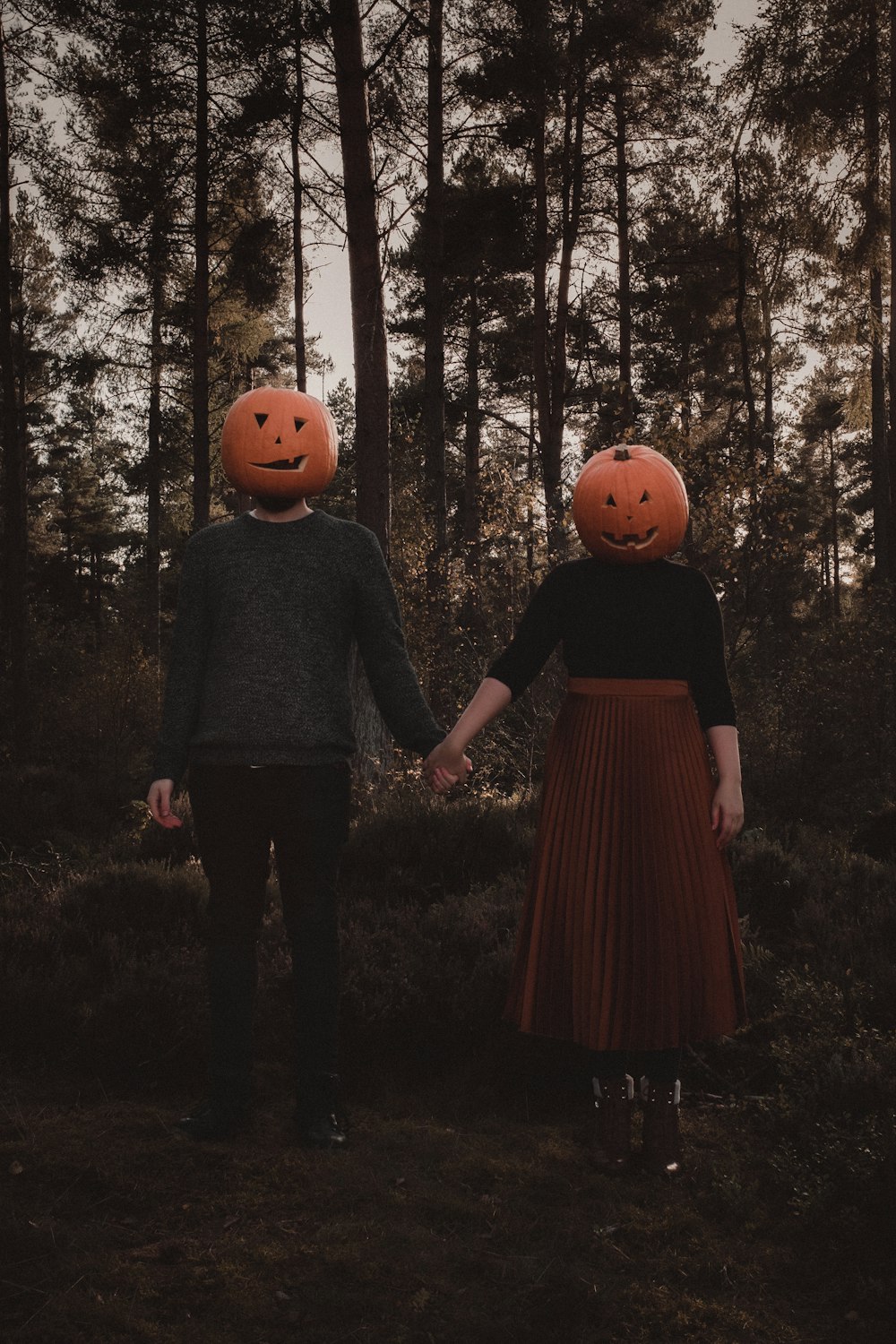 a man and a woman holding hands with pumpkins on their heads