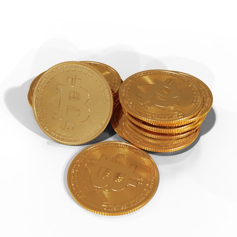 A collection of shiny, gold-colored coins featuring a prominent Bitcoin symbol on each. The coins are stacked and scattered on a white background.