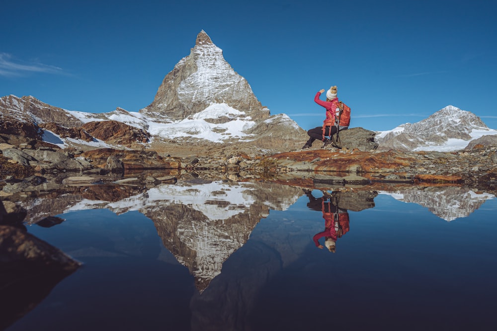 a man standing on top of a mountain next to a lake