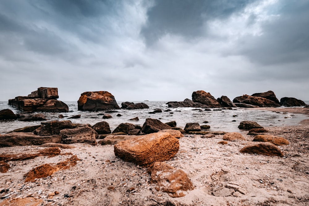 a beach with rocks and water under a cloudy sky