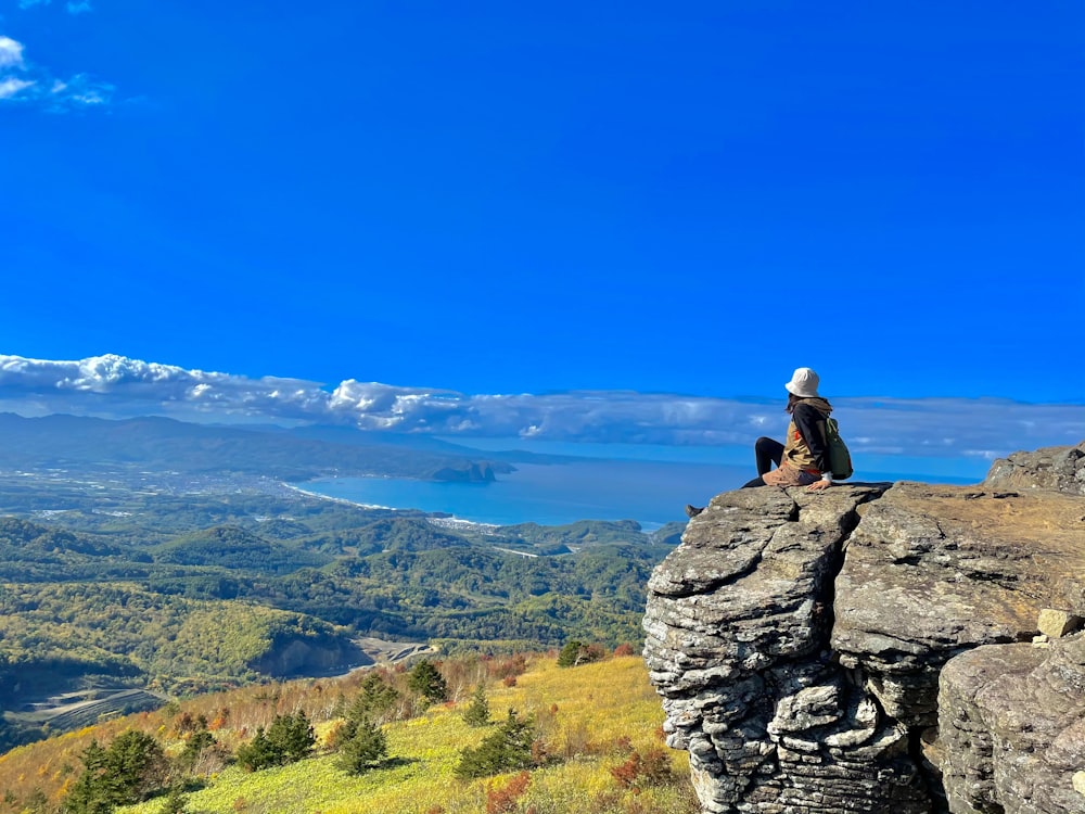 une personne assise au sommet d’un gros rocher