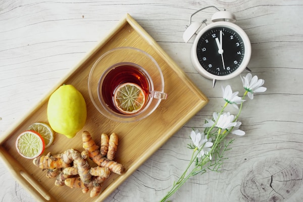 A cup of tea with lemon and ginger on a tray next to a clock