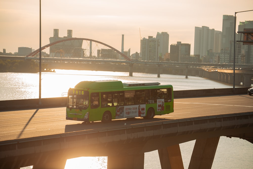a green bus driving over a bridge over water
