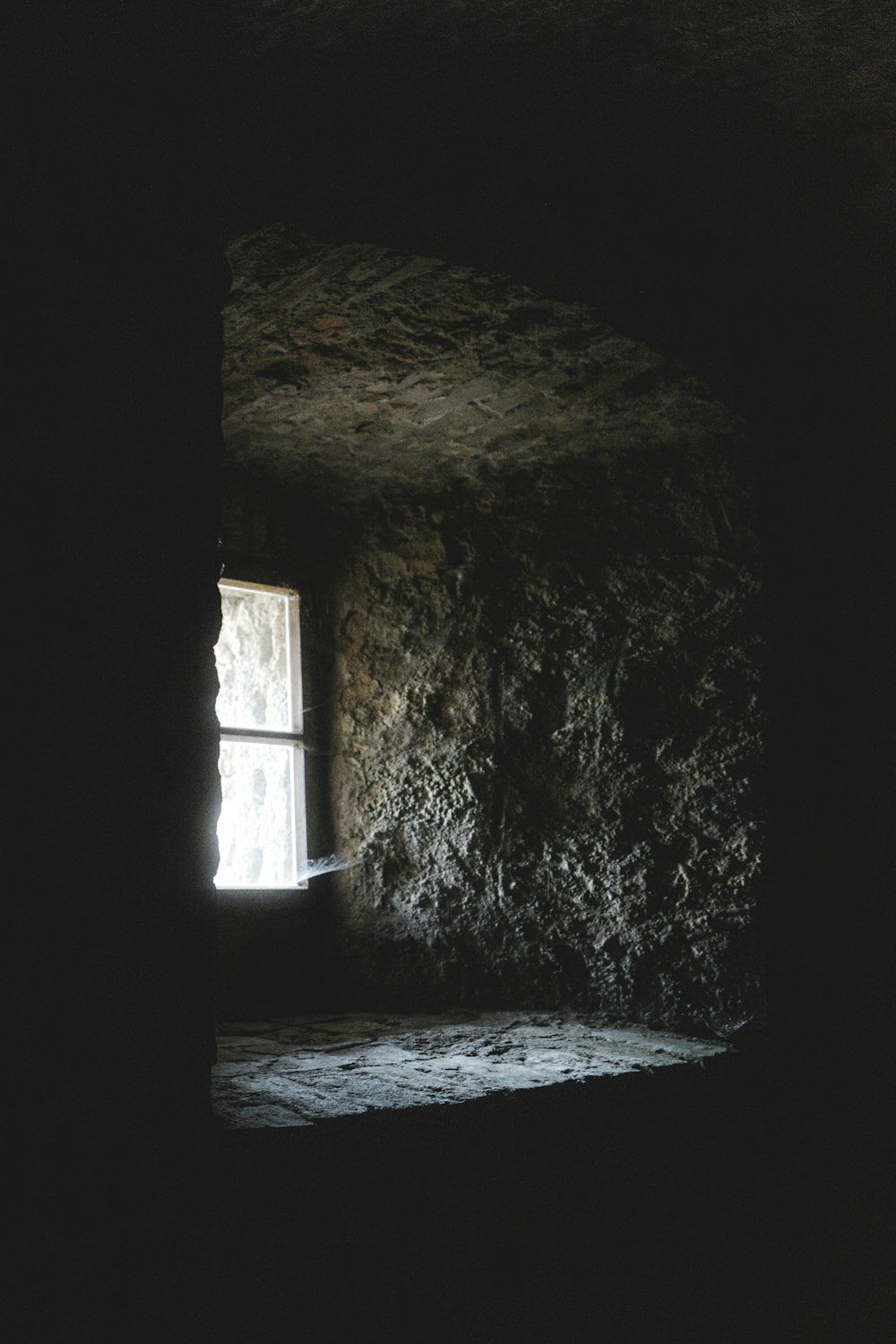 a dark room with a window and a stone wall