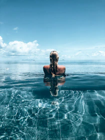 a woman is sitting in the water with her back to the camera
