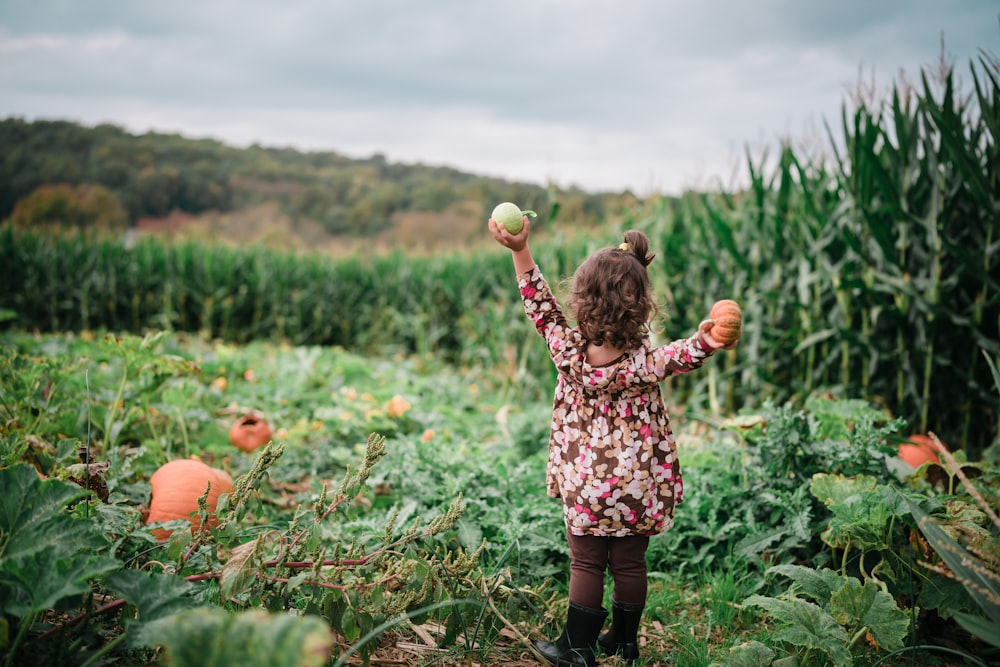 a little girl holding a green apple in a field